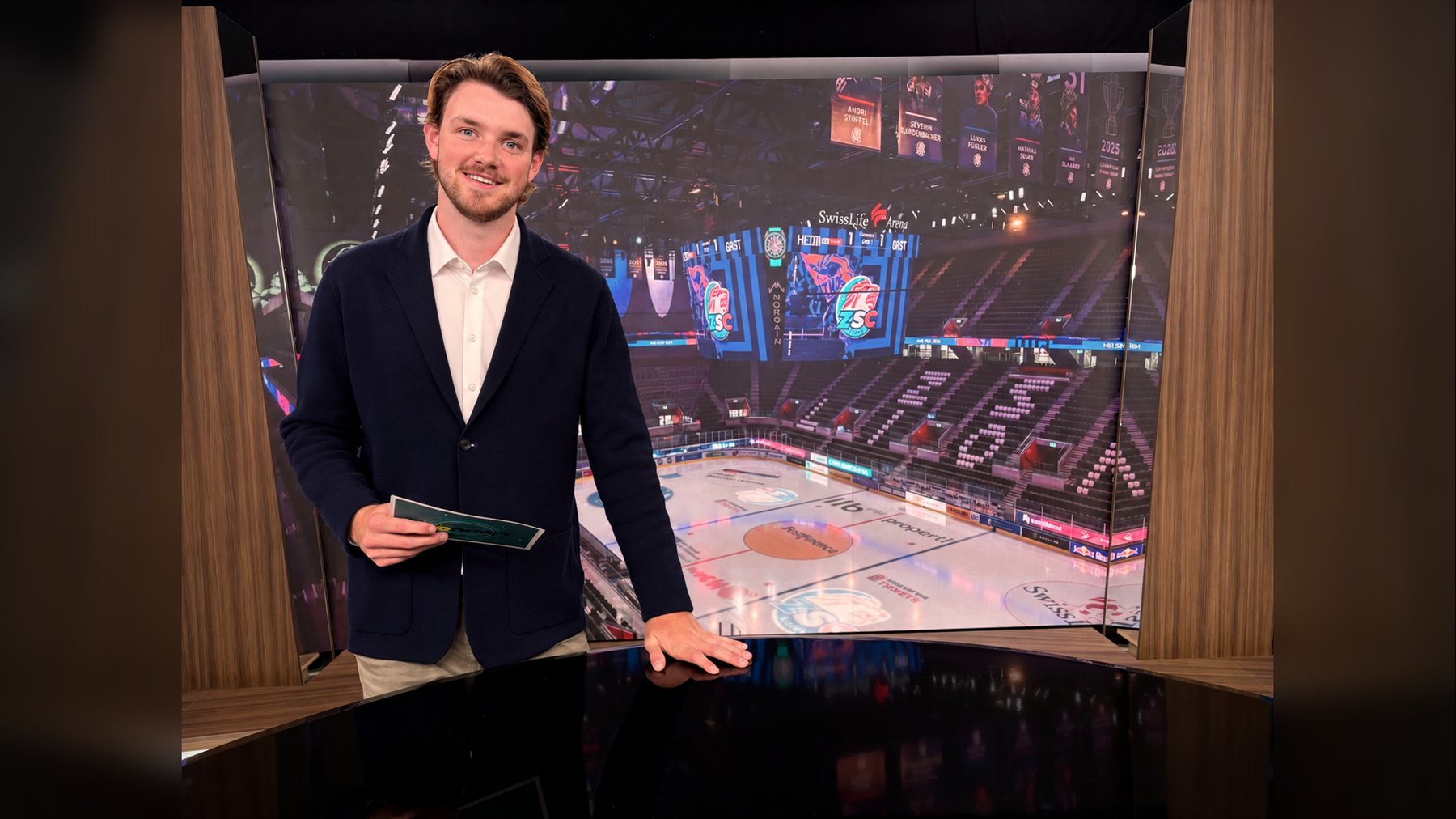 Romeo Marchesi im Fernsehstudio vor einer Grossbildwand mit einer Eishockeyarena